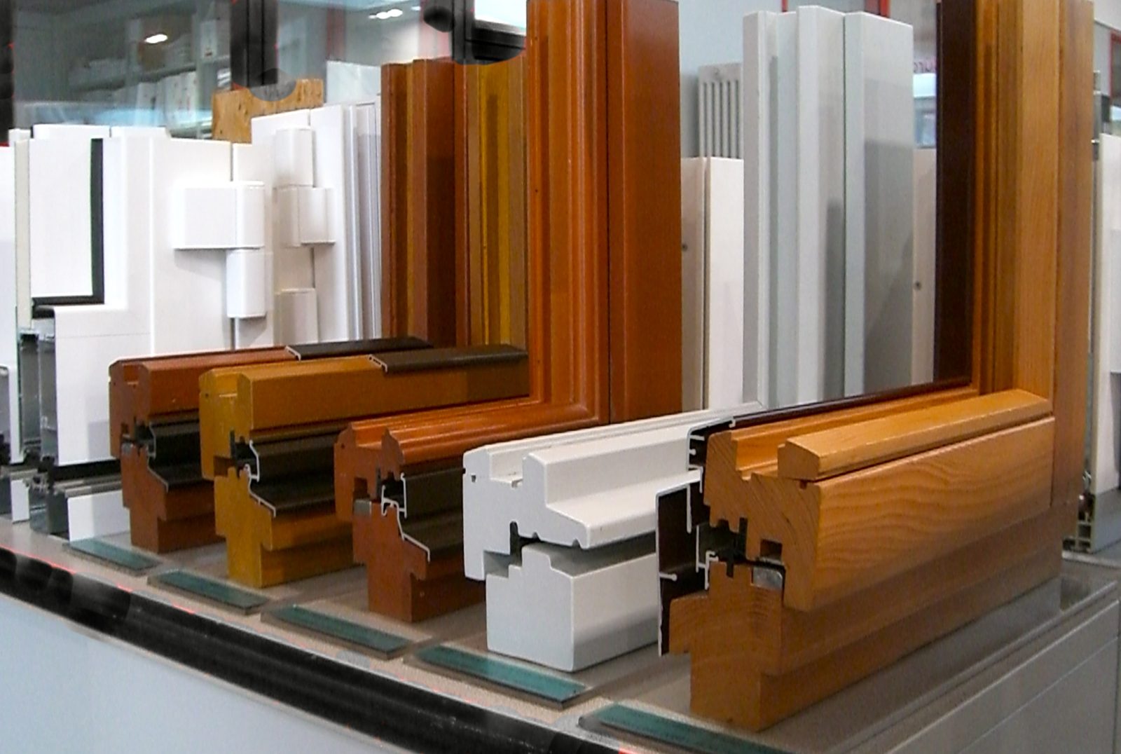 Staalmodellen van raamprofielen in wit kunststof en verschillende houtkleuren, naast elkaar uitgestald